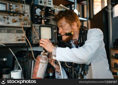 Crazy scientist conducting an experiment in laboratory. Electrical testing tools on background. Lab equipment, engineering workshop