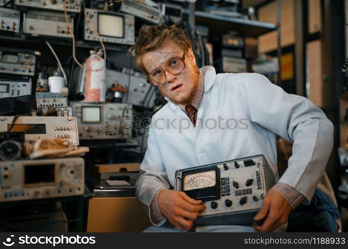 Crazy scientist holds electrical device in laboratory. Electrical testing tools on background. Lab equipment, engineering workshop. Crazy scientist holds electrical device in lab
