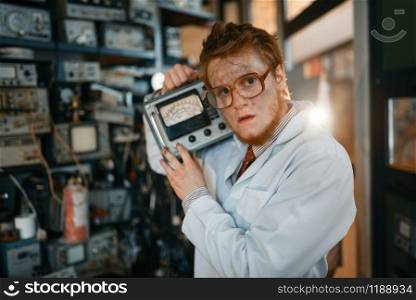Crazy scientist in glasses holds electrical device in laboratory. Electrical testing tools on background. Lab equipment. Scientist in glasses holds electrical device