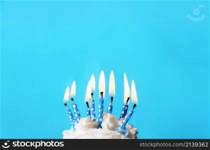 cream cake with blue candles on top, the candles have white dots and are lit. before a light blue background.