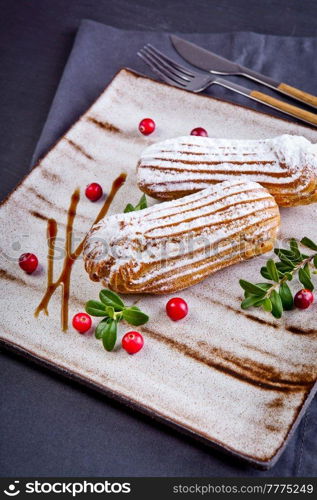 Cream eclairs choux pastries served with fresh cranberries on a handmade ceramic plate