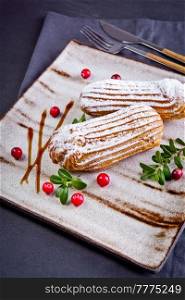 Cream eclairs choux pastries served with fresh cranberries on a handmade ceramic plate