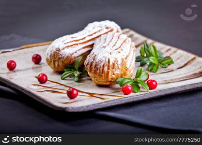 Cream eclairs choux pastries served with fresh cranberries on a handmade ceramic plate