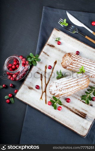 Cream eclairs choux pastries served with fresh cranberries on a handmade ceramic plate