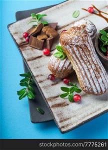 Cream eclairs choux pastries served with fresh cranberries on a handmade ceramic plate