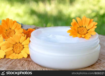 Cream for body care with calendula. Fresh orange calendula flowers on a wooden background in nature. Cosmetic cream for cleansing the skin with calendula flowers. Medical Dermatology.. Cream for body care with calendula. Fresh orange calendula flowers on a wooden background in nature. Cosmetic cream for cleansing the skin with calendula flowers.