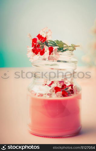 Cream in glass jar for skin care with flowers at turquoise background, front view. Beauty, natural cosmetic, spa or body care concept