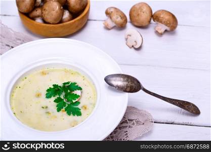 Cream mushroom soup of fresh champignons in a round white plate with an iron spoon