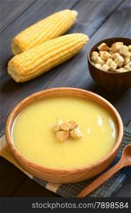 Cream of corn soup in wooden bowl with croutons on top, photographed on dark wood with natural light (Selective Focus, Focus on the front of the croutons on the soup)