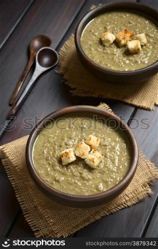 Cream of lentil soup in rustic bowls with croutons on top, wooden spoons on the side, photographed on dark wood with natural light (Selective Focus, Focus on the front of the croutons on the first soup)