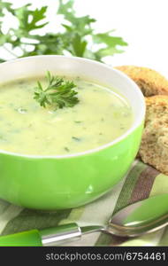 Cream of potato with herbs and green onions garnished with parsley and served in a green bowl with bun and parsley (Selective Focus, Focus on the front of the parsley in the soup). Potato Soup with Herbs