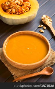 Cream of pumpkin soup served in wooden bowl, photographed on dark wood with natural light (Selective Focus, Focus on the middle of the soup)