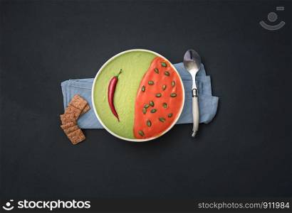Cream soup bowl with crackers on black background. Red and green soup plate. Tomato and spinach cream soup. Flat lay of healthy food. Vegetarian meal