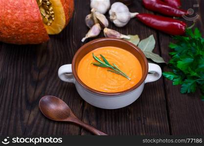 cream soup of fresh pumpkin in a ceramic plate, next to the ingredients and a wooden spoon, top view