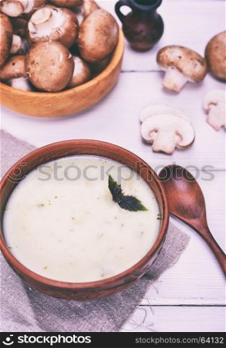 Cream soup with champignons in a brown clay plate on a white table, close up