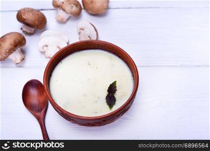 cream soup with mushrooms in a round clay plate on a white wooden background, view from above