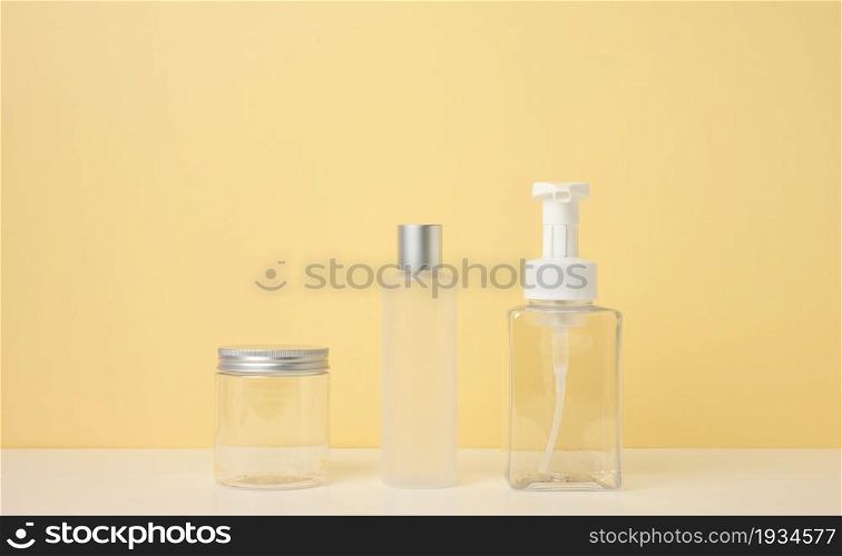 cream tubes, cosmetic dispenser, empty plastic jar, transparent dispenser on a light yellow background. Branding of cosmetic products, mock up
