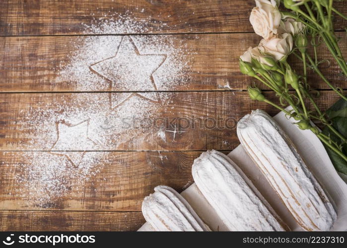 creamy baked eclairs with pink roses with stars drawn sugar powder wooden desk