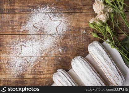 creamy baked eclairs with pink roses with stars drawn sugar powder wooden desk