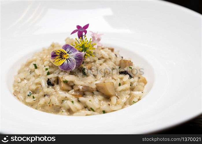 Creamy cheese risotto with mushroom and truffle oil decorate with yellow and purple flower. International italian gourmet cuisine a la carte in buffet live station. Using for food and drink industry.. Risotto