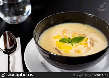 Creamy chicken soup on a black plate on a dark background.
