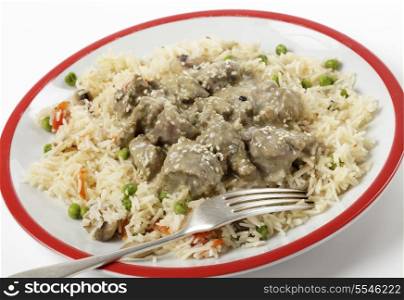 Creamy lamb korma curry garnished with toasted sesame seeds and served on a bed of vegetable pilau, with a fork.