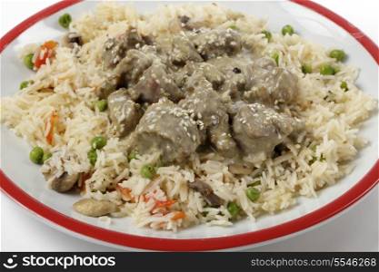 Creamy lamb korma curry garnished with toasted sesame seeds and served on a bed of vegetable pilau, close-up