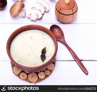 Creamy mushroom soup in a brown round plate with a wooden spoon on a white background, top view