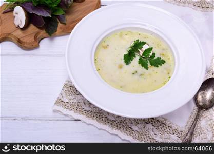Creamy mushroom soup in a white round plate on a white wooden background, top view