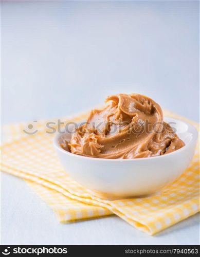 Creamy peanut butter in white bowl over yellow napkin, selective focus, copy space