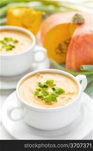 Creamy pumpkin bacon soup with green onion in two white bowls, autumn cuisine