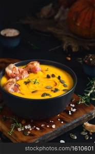 Creamy pumpkin soup with fried bacon slices with cream and pumpkin seeds in black bowl on black wooden table. Close-up, selective focus. Ingredients for making seasonal pumpkin soup on the table