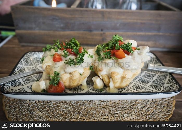 Creamy tartlets with chicken and asparagus sauce topped with parsley on a plate on a wooden table in a restaurant serving food