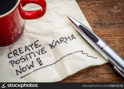 create positive karma now - motivational handwriting on a napkin with cup of coffee