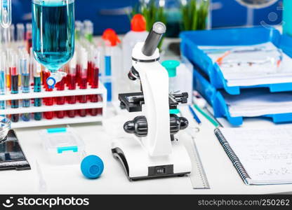 Creative abstract chemistry development, medicine, pharmacy, biology, biochemistry and research technology concept: table with scientific chemical laboratory equipment - microscope, test tubes with color liquid substance samples, vials, flasks, report documents etc. with selective focus effect