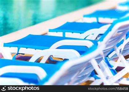 Creative abstract travel, tourism and summer vacation holidays activity concept: macro view of chaise longue beach chairs and swimming pool with blue water in tropical spa resort hotel with selective focus effect