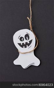 Creative application handcraft from white paper with decorative terrible spirits smiling on a black background, place for text. Halloween concept. Flat lay.. Halloween greeting card with laughing flying scary Casper hanging from a rope handmade from paper on a black .