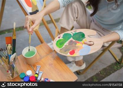 Creative art concept, Female artist is washing paintbrush while painting art on canvas in garden.