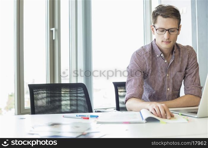 Creative businessman reading file at desk in office