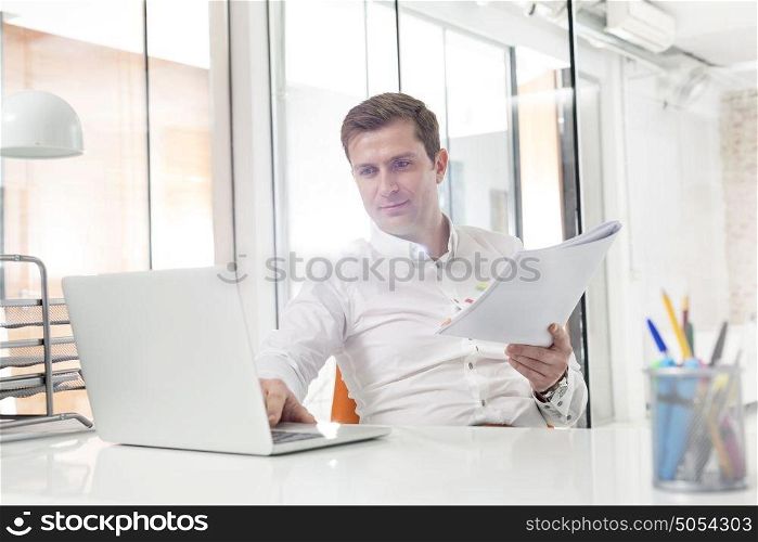 Creative businessman with laptop and documents in office
