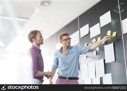 Creative businessmen discussing over sticky paper on wall in office