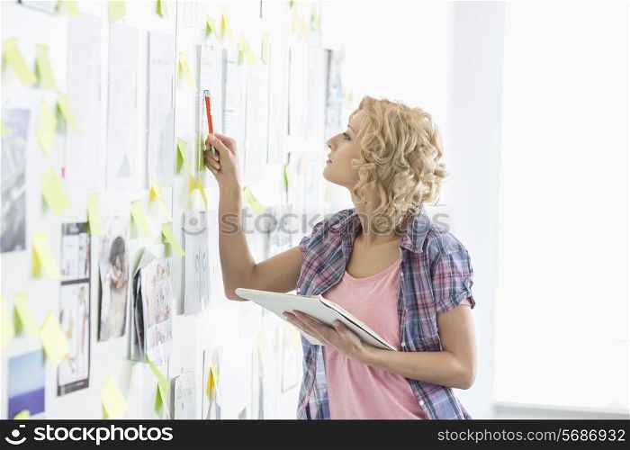Creative businesswoman analyzing papers stuck on wall in office