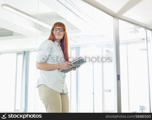 Creative businesswoman looking away while holding files in office