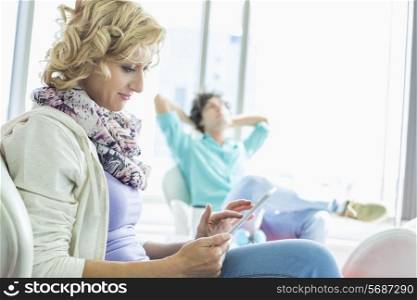 Creative businesswoman using digital tablet at lobby with colleague relaxing in background