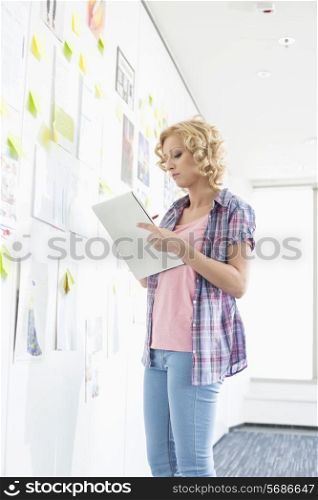 Creative businesswoman writing notes by papers stuck on wall in office