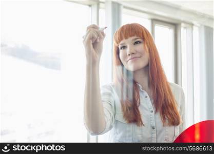 Creative businesswoman writing on glass wall in office