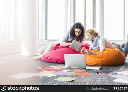 Creative businesswomen using tablet PC while relaxing on beanbag chairs at office