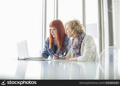 Creative businesswomen working on laptop together in office