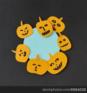 Creative card for invitation for Halloween with handmade paper round frame and yellow smiling scary pumpkins on a black paper, place under text. Flat lay. Decorative round blue Halloween frame handcraft with paper laughing pumpkin on a black paper background.