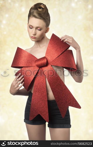 creative christmas portrait of sexy woman adorned like a gift with big red bow on the breast and elegant hair-style